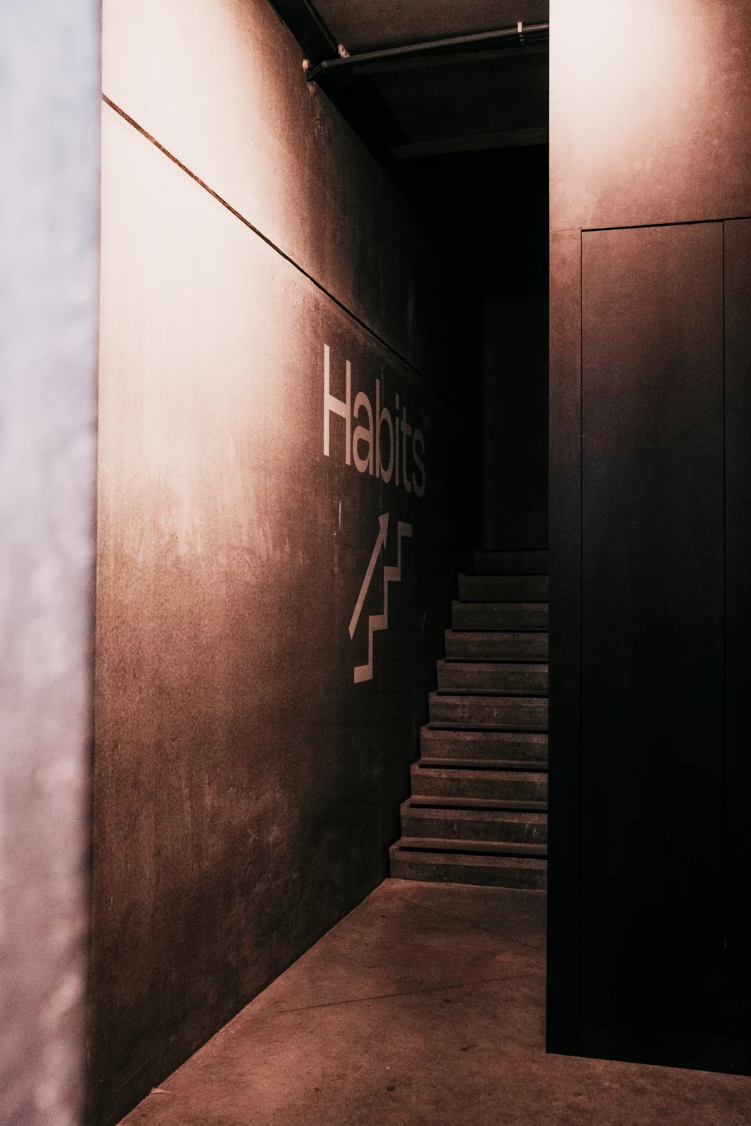 Het Habits-logo op de terracotta wand bij de trap
