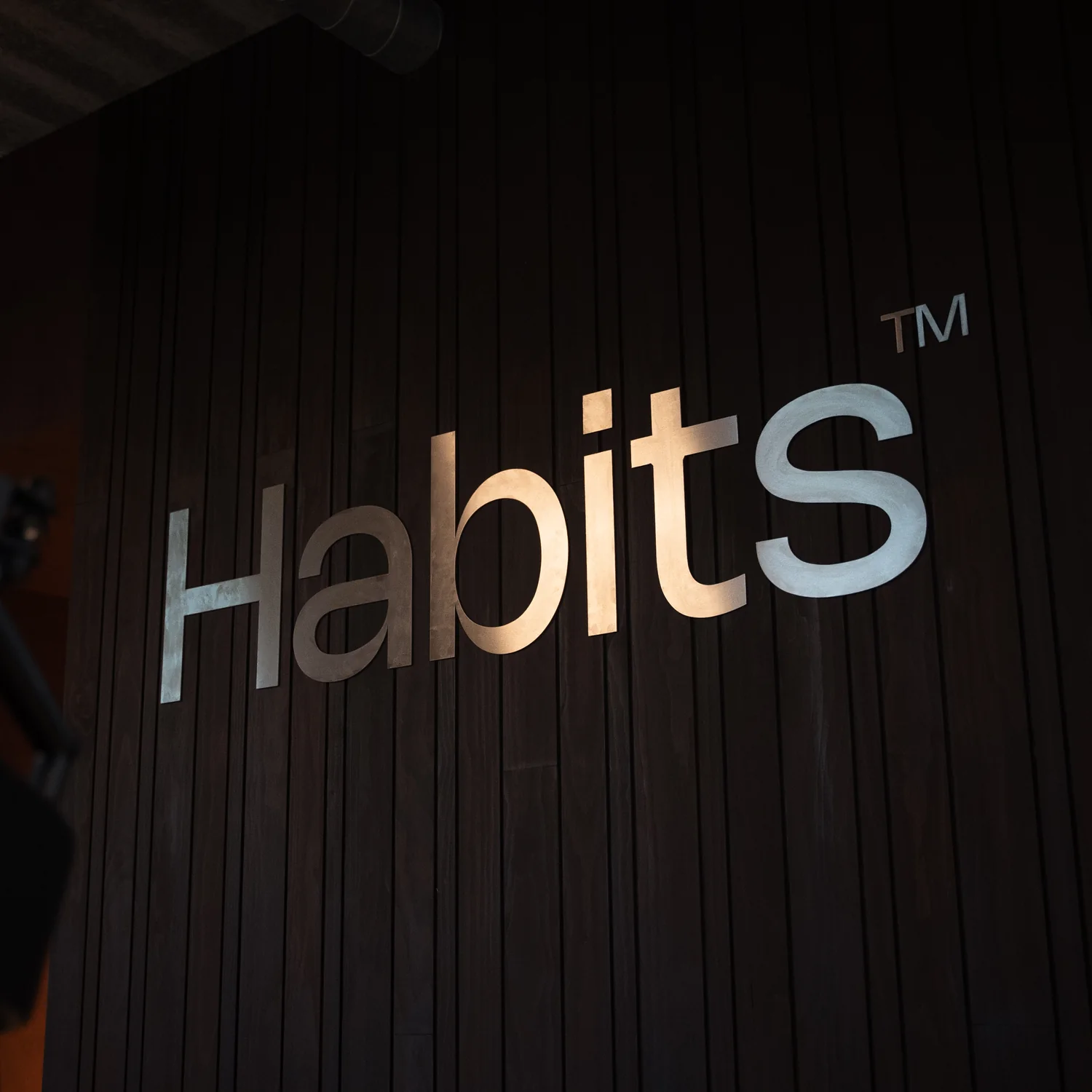 Het Habits-woordmerk in metaal op een donkere houten wand