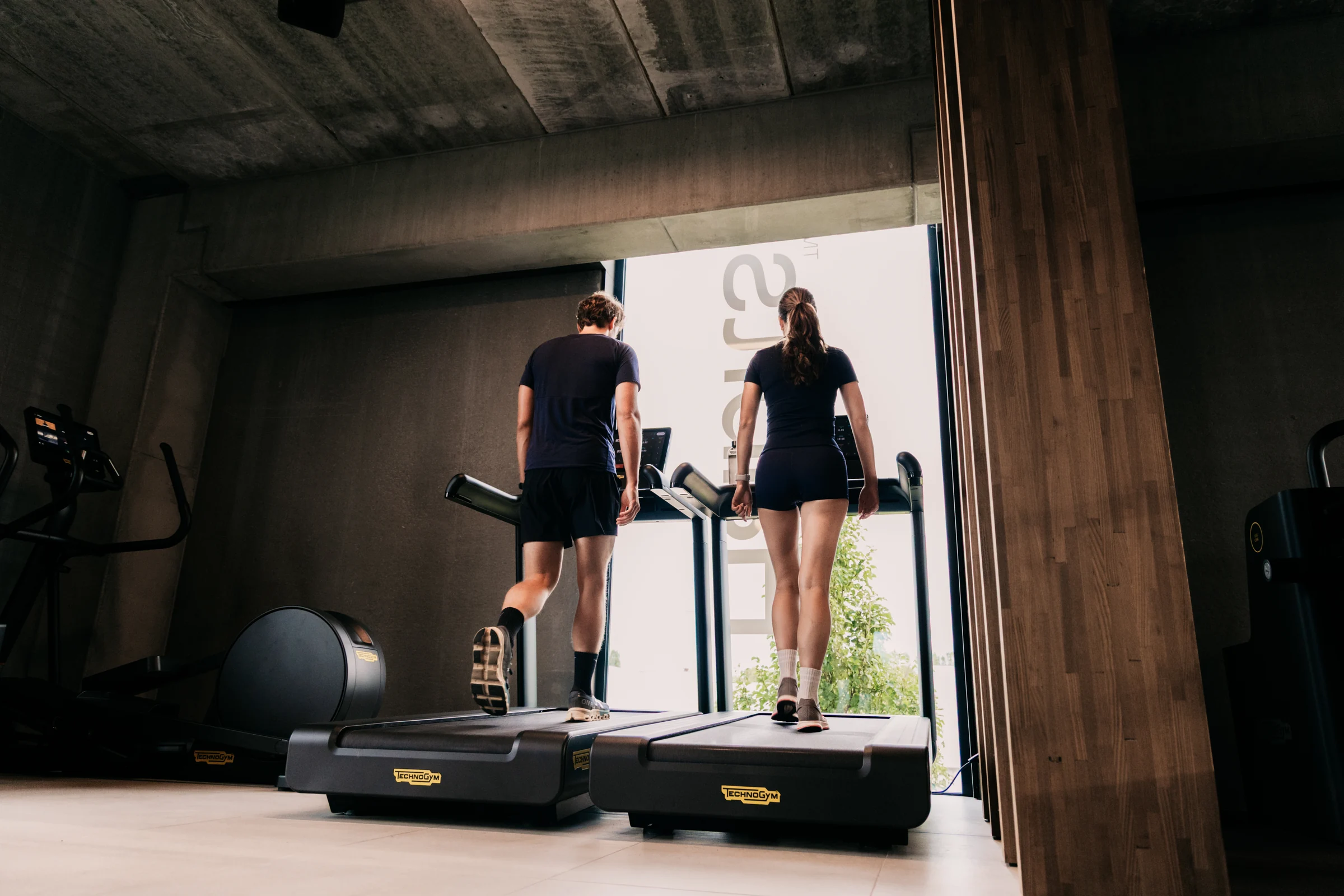 Twee leden trainen naast elkaar op de loopbanden aan het raam bij Habits