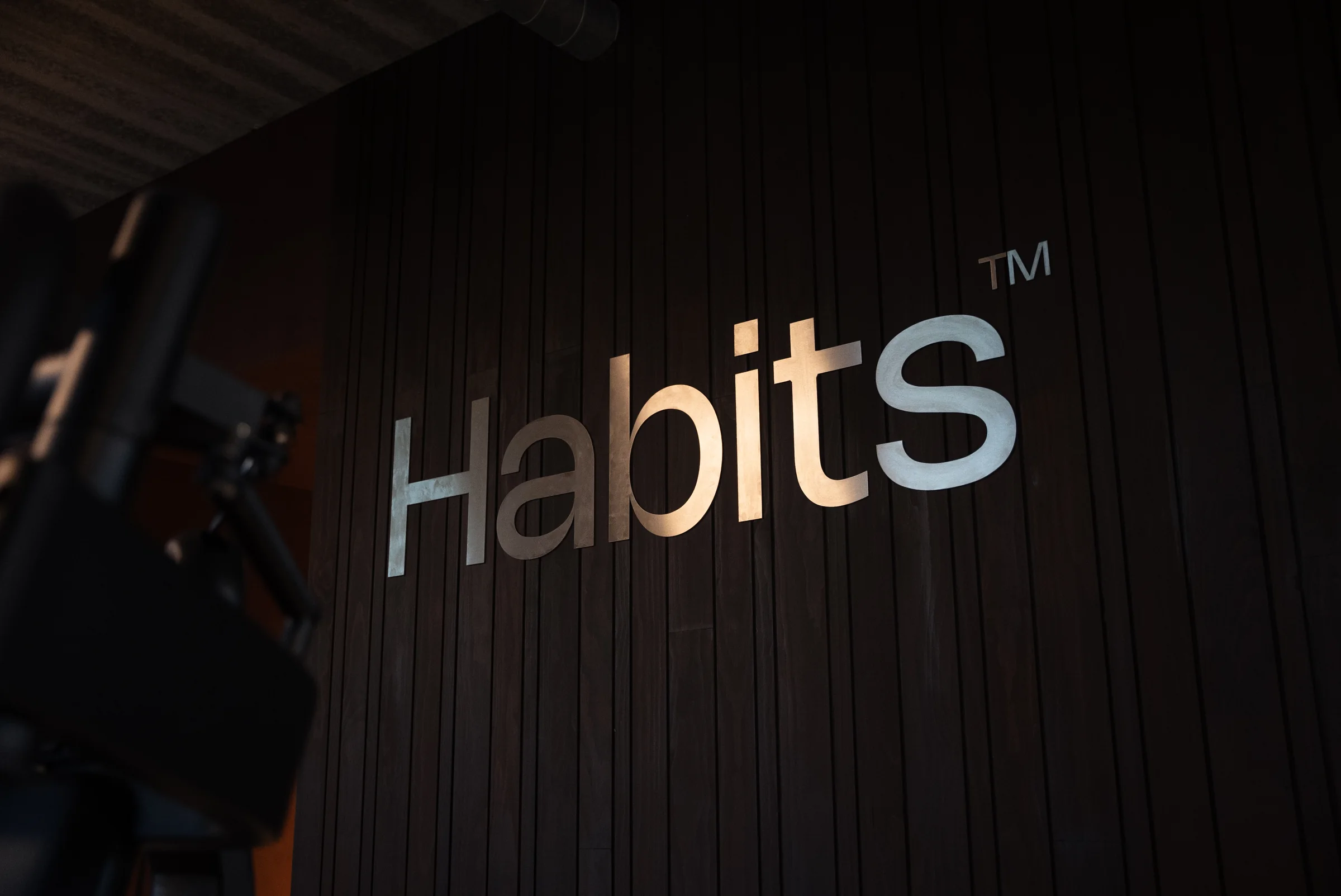 Het Habits-woordmerk in metaal op de donkere houten wand van de club